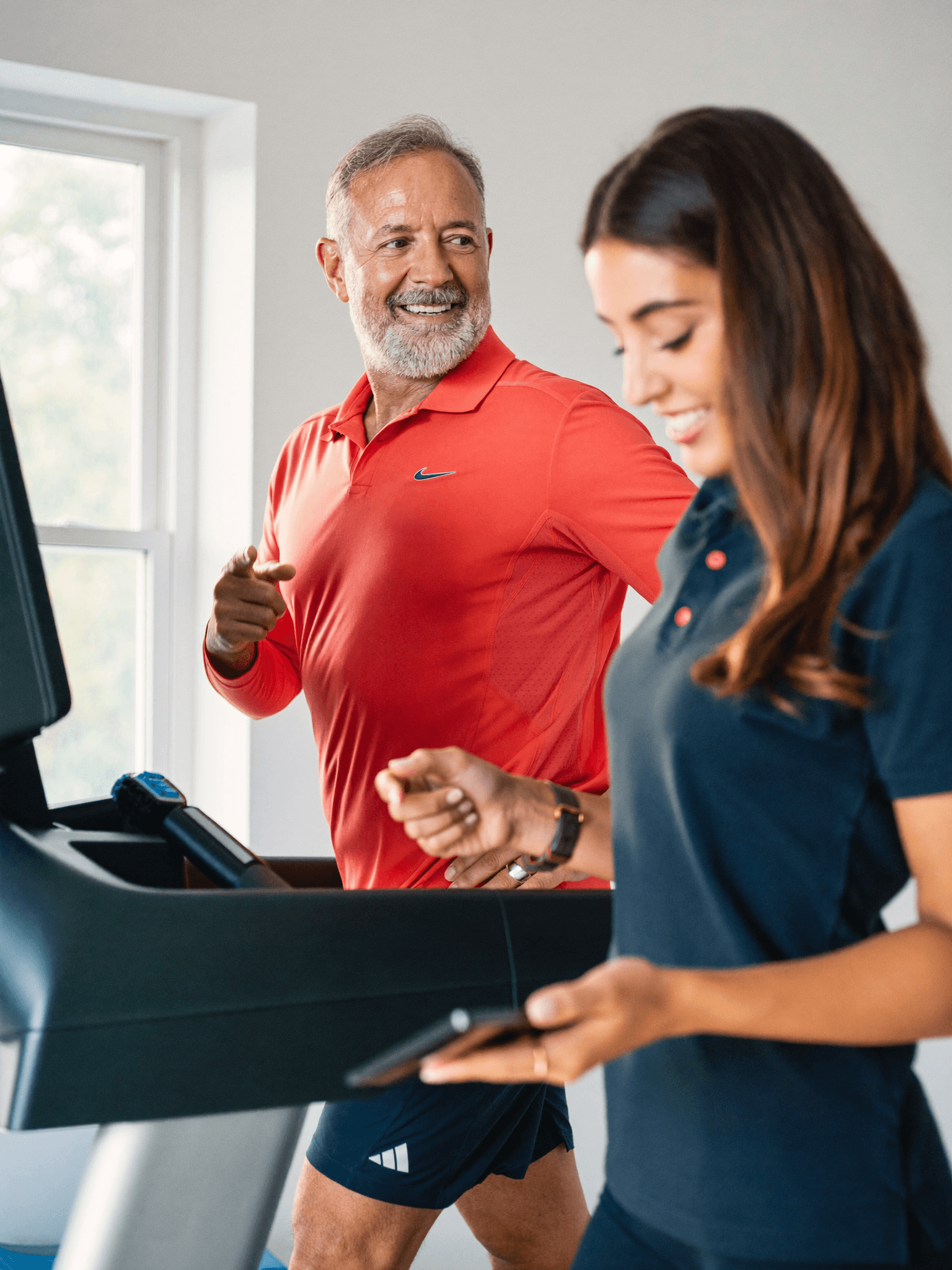 A cardiac exercise coach reviews live wearable data on a tablet while her client walks a monitored treadmill session